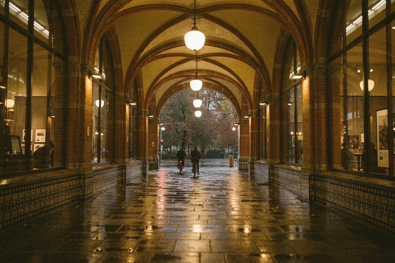 Cyclists riding through the vaulted, tiled passage beneath the Rijksmuseum on a wet evening