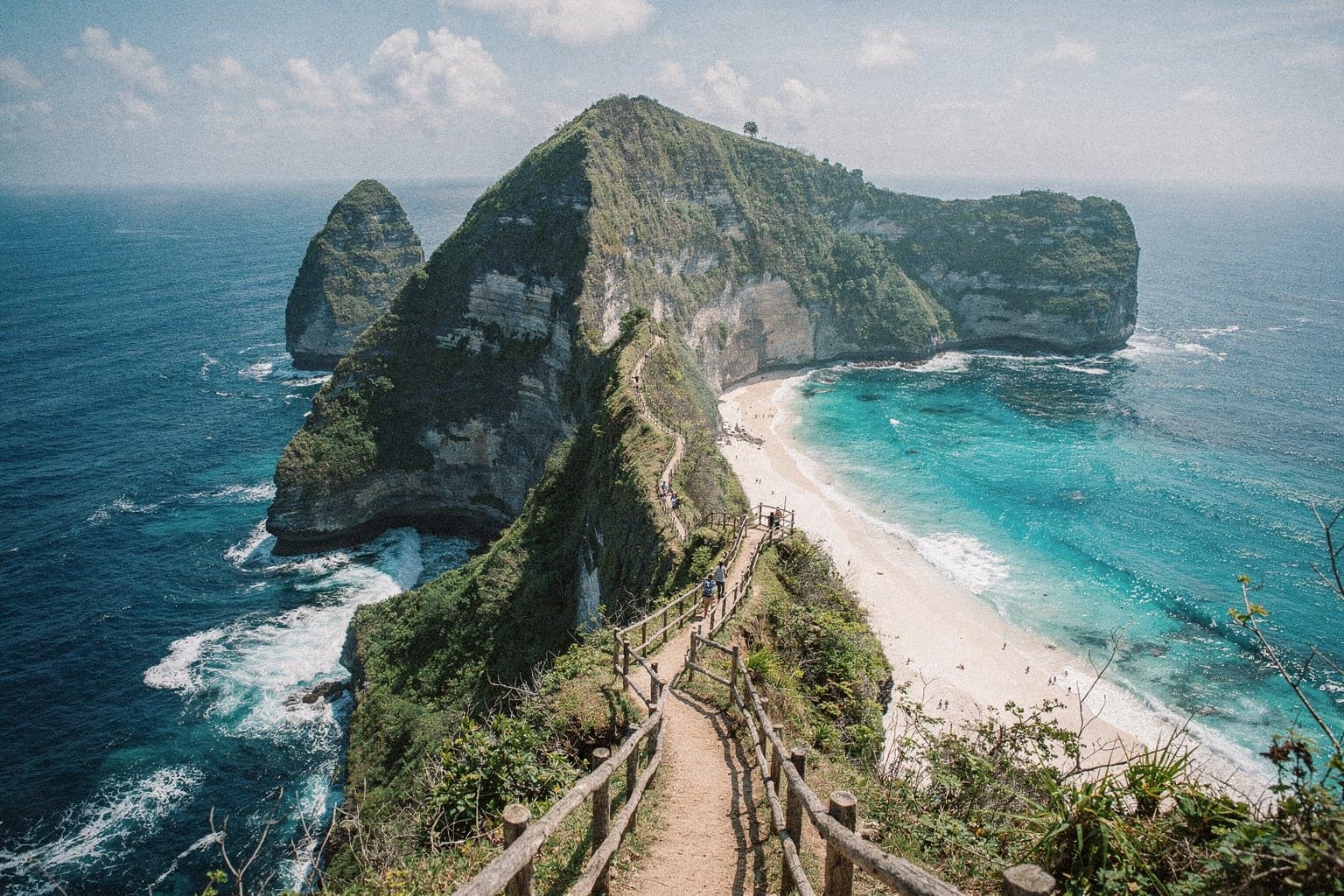Kelingking Beach on Nusa Penida seen from the clifftop, the steep green headland dropping to a crescent of white sand and turquoise water