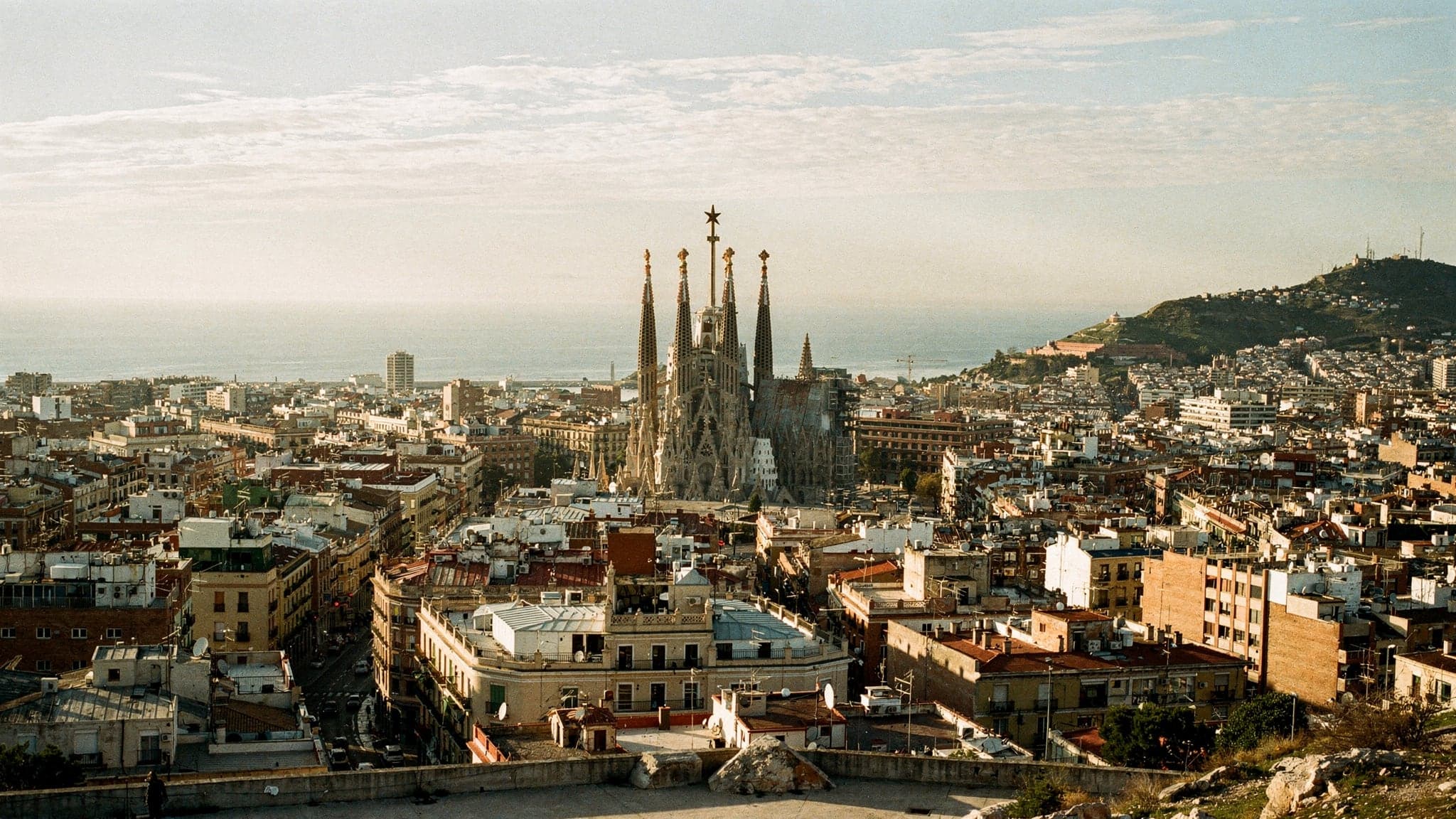 Barcelona from the Bunkers del Carmel in late-afternoon light, the Eixample grid running down to the sea with the Sagrada Família's towers rising in the middle