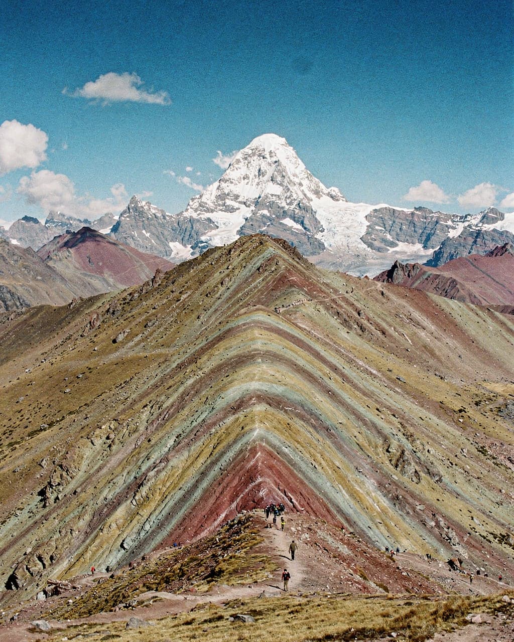 Striped red, ochre and turquoise ridges of Vinicunca Rainbow Mountain with snow-capped Ausangate on the horizon