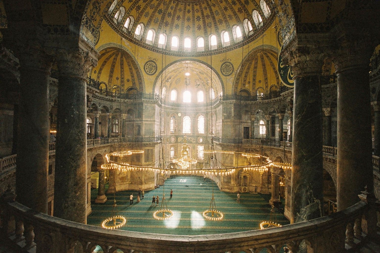 Inside Hagia Sophia from the upper gallery, with the great dome, hanging lamps and the carpeted prayer hall below