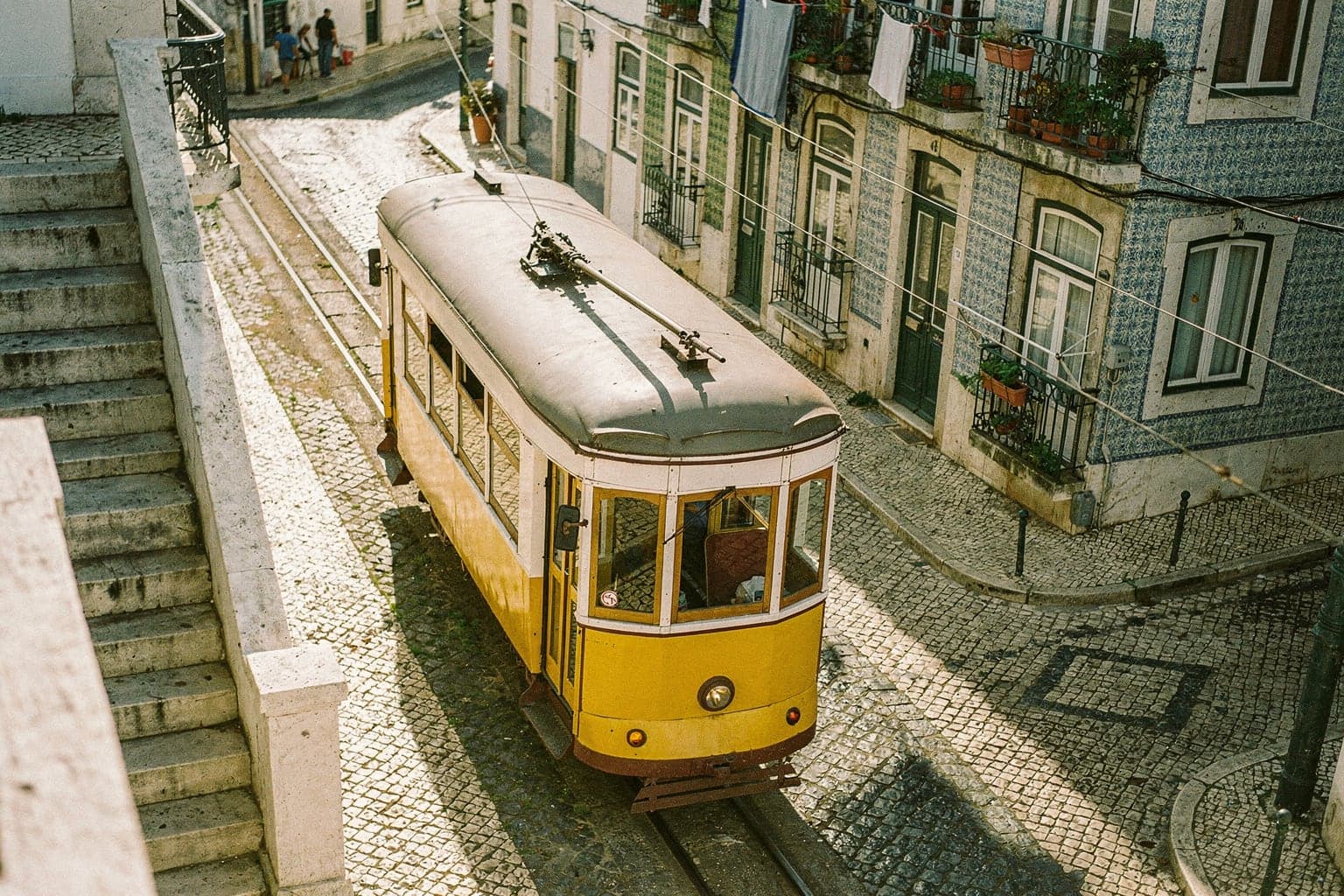 A yellow Tram 28 climbing a narrow cobbled street in Graça past blue and green tiled façades