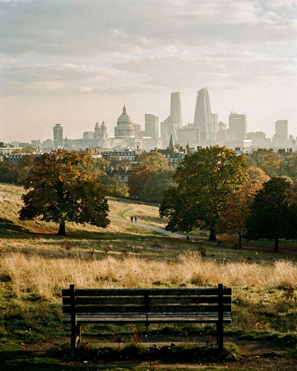 Parliament Hill on Hampstead Heath in late-afternoon autumn light, looking south over grassland to the city skyline