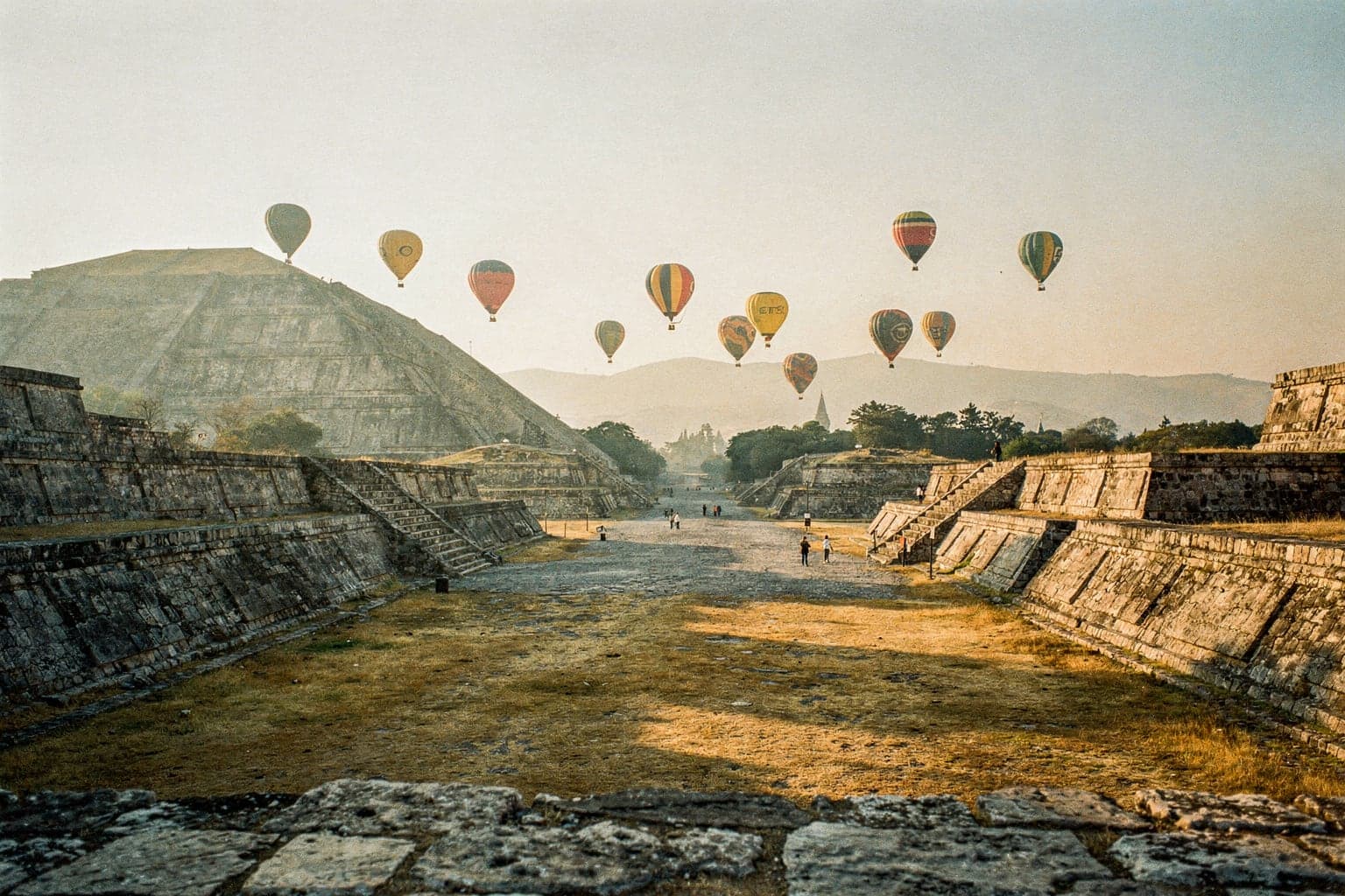 Teotihuacán at sunrise from the Plaza of the Moon, looking down the Avenue of the Dead to the Pyramid of the Sun, with hot-air balloons overhead