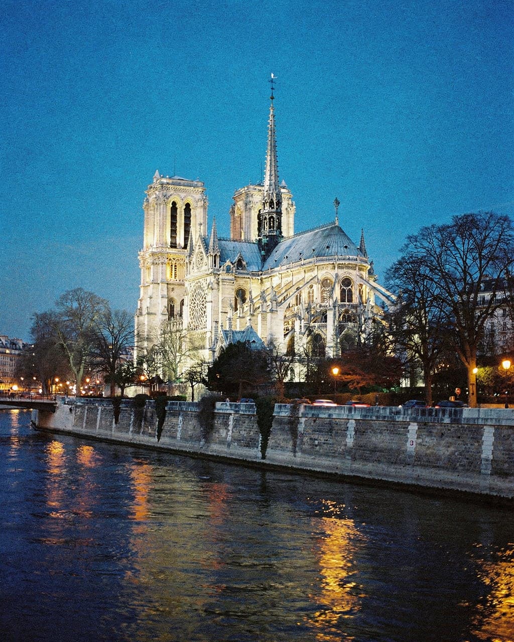 Notre-Dame de Paris at blue hour seen from the Left Bank, its flying buttresses and restored spire softly lit above the Seine
