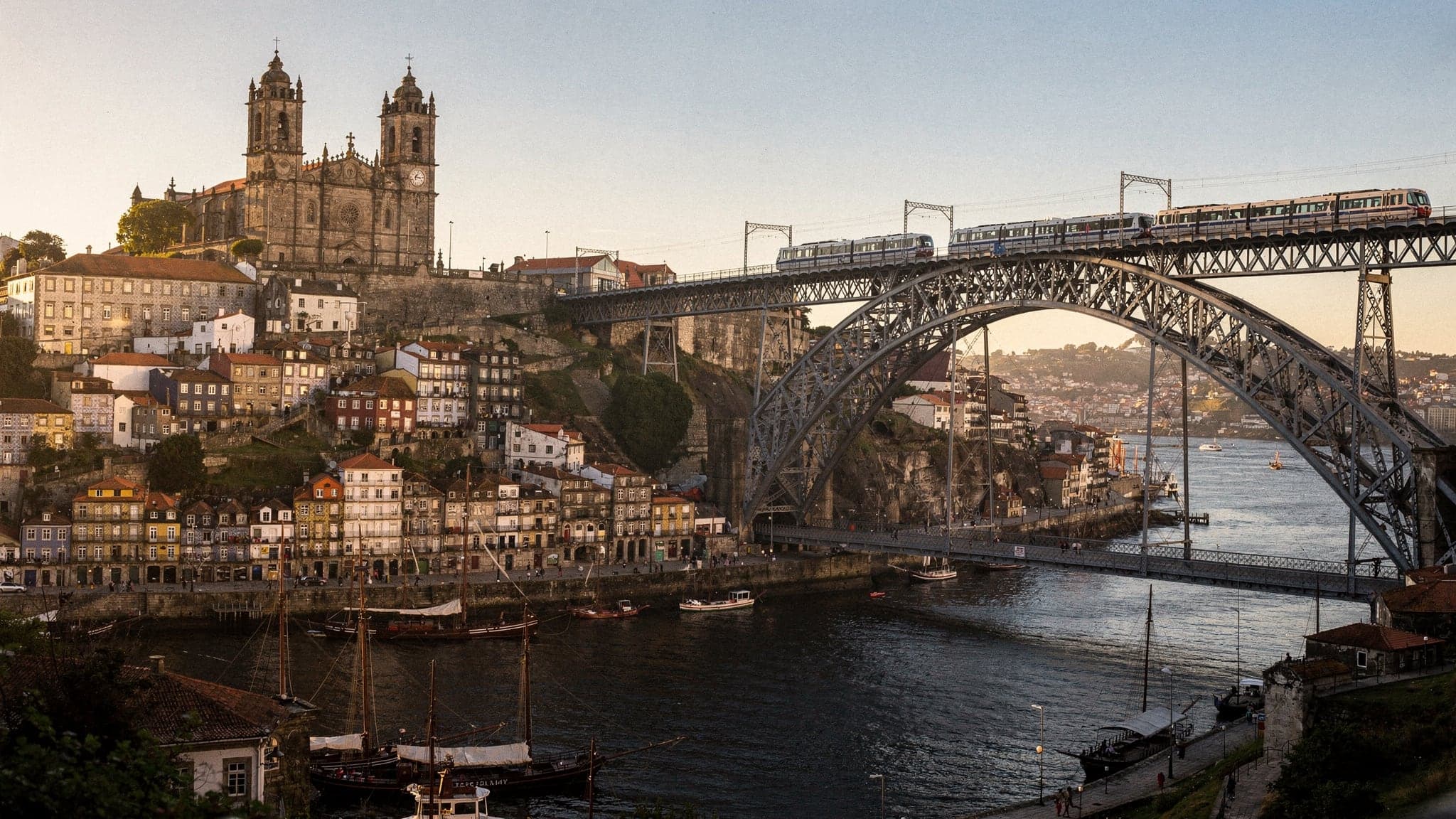 Porto's stacked riverside houses and the cathedral on its hill across the Douro at golden hour, seen from the Jardim do Morro beside the Dom Luís I Bridge