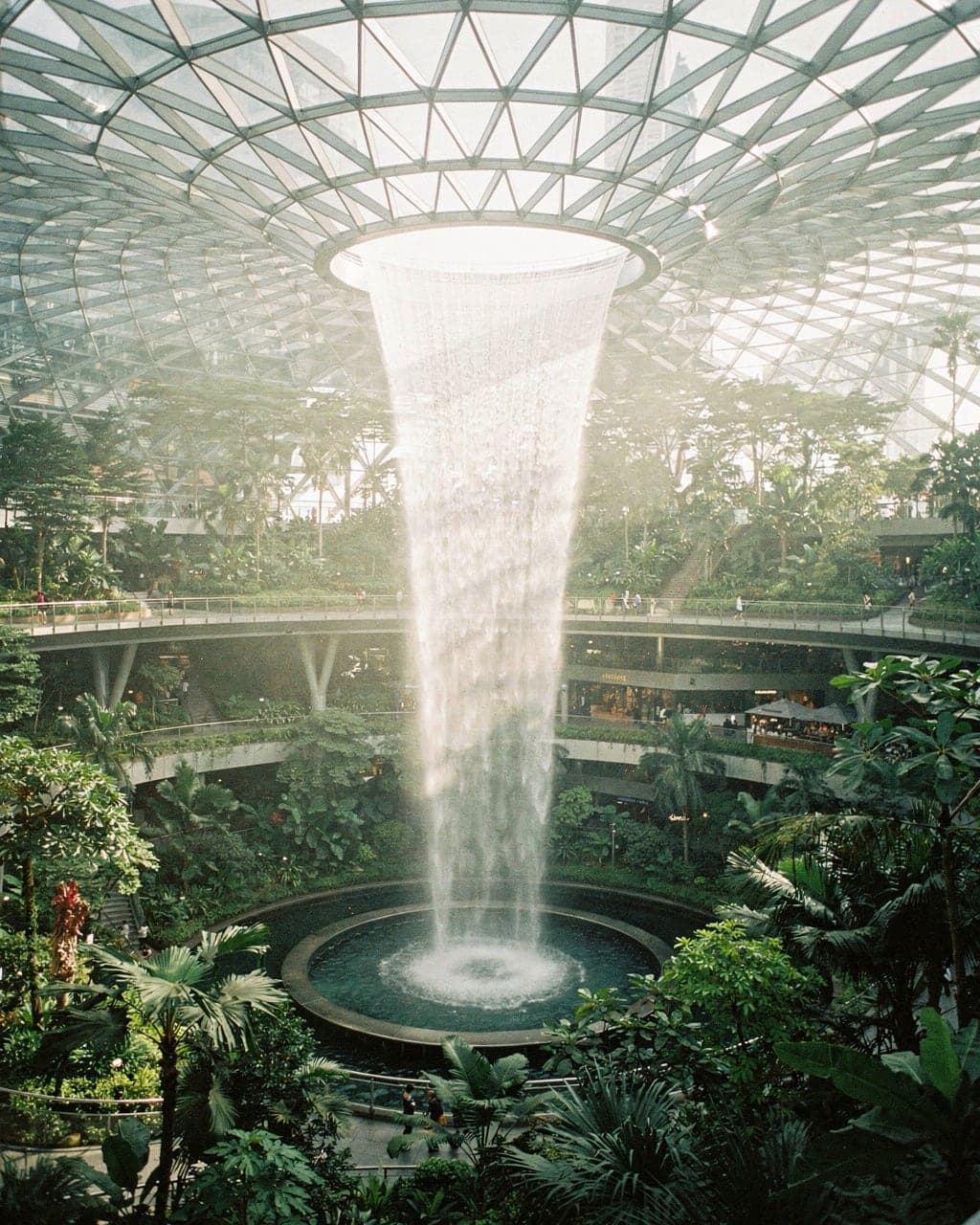 The Rain Vortex waterfall pouring through the glass dome of Jewel Changi Airport into a terraced indoor forest