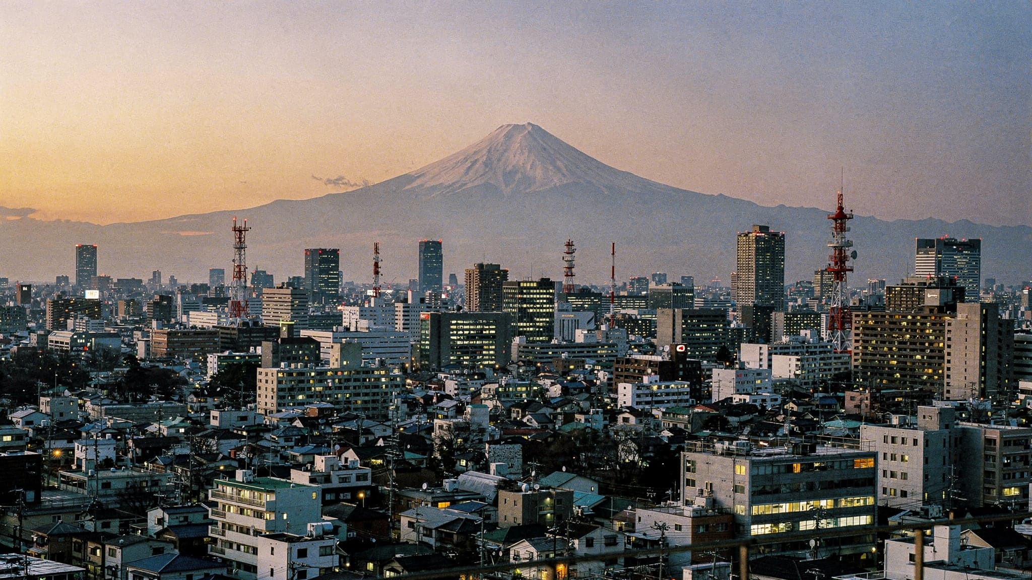 The Tokyo skyline at winter dusk seen from a Shinjuku tower, with the snow-capped cone of Mount Fuji silhouetted on the western horizon