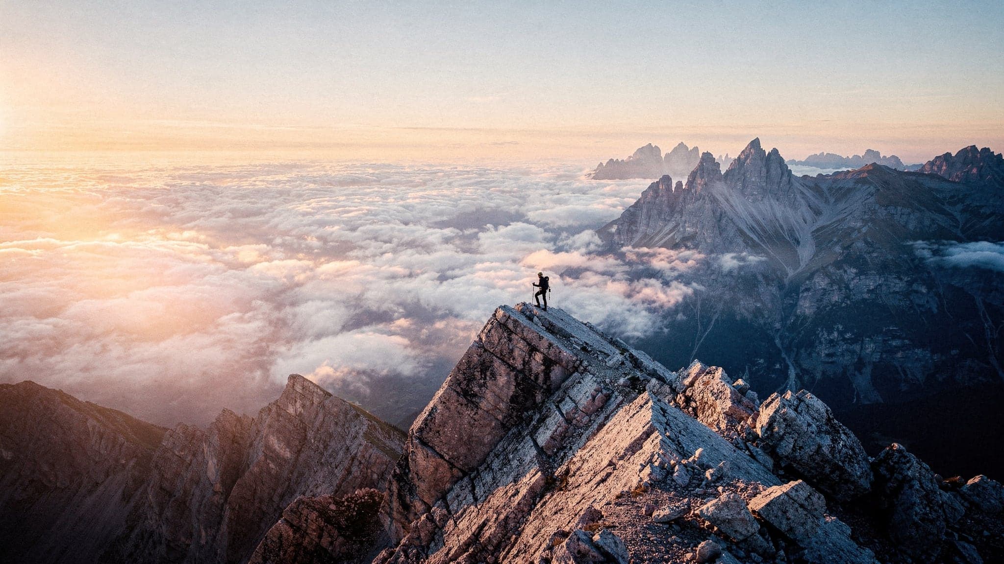 A hiker on a sharp granite ridge above a sea of clouds at sunrise in the Dolomites